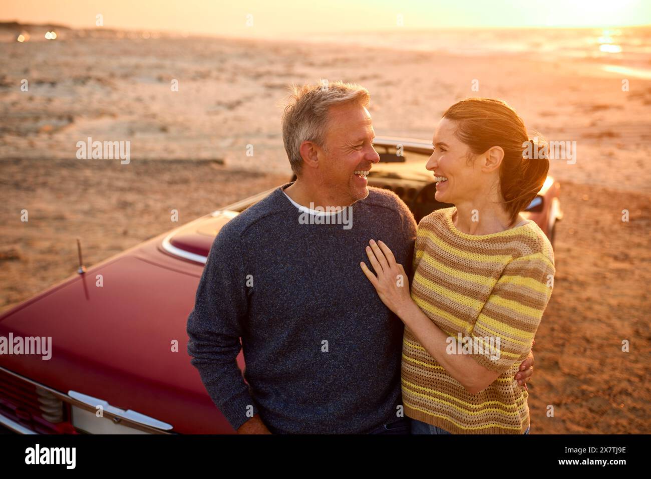 Adorabile coppia senior in pensione in vacanza accanto a Classic Sports Car at Beach Watching Sunrise Foto Stock