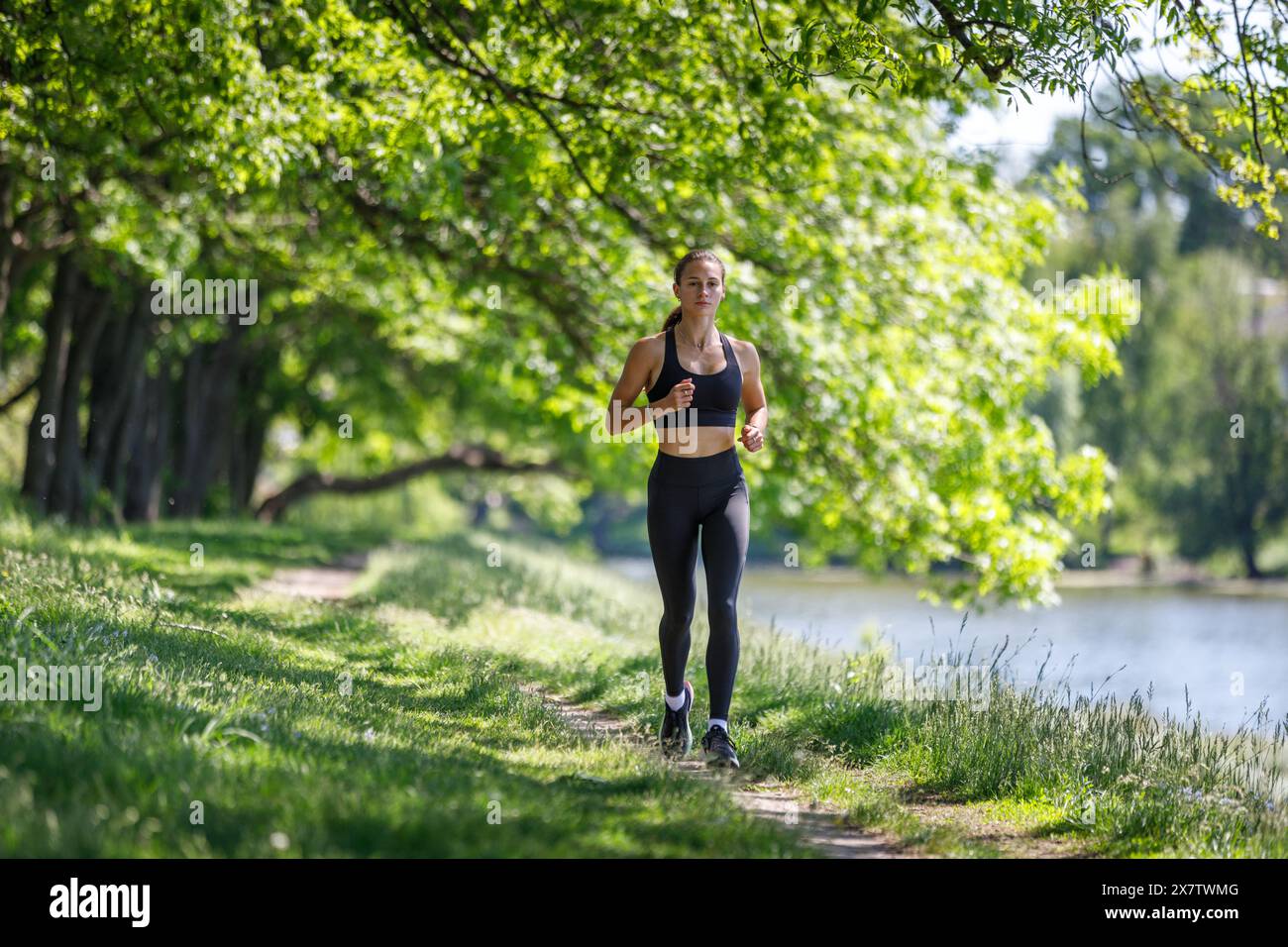 Giovane donna fitness che fa jogging nel parco porta il fiume al mattino di sole. Ragazza sportiva che corre nel parco Foto Stock