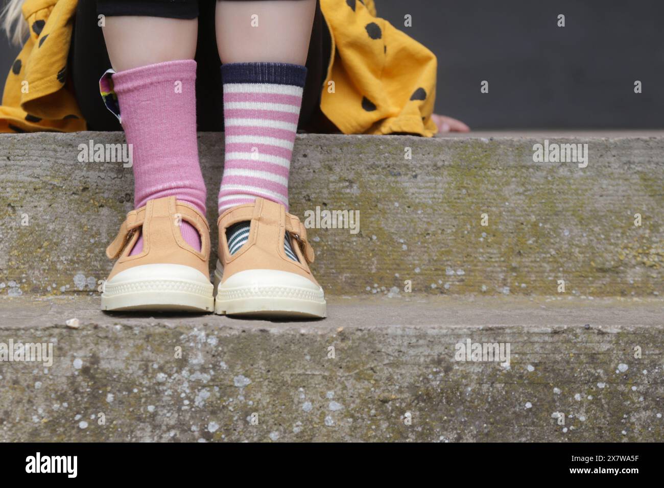 Il ragazzo indossa un paio diverso di calzini. Il bambino si allena in calze non abbinate in piedi all'aperto. Concetto di consapevolezza della sindrome di Down, giornata di calzini strani, erba anti-bullismo Foto Stock