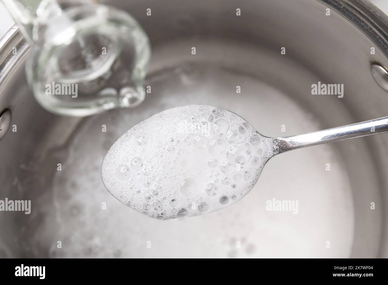 Versare l'aceto nel cucchiaio con bicarbonato di sodio sulla pentola, closeup Foto Stock