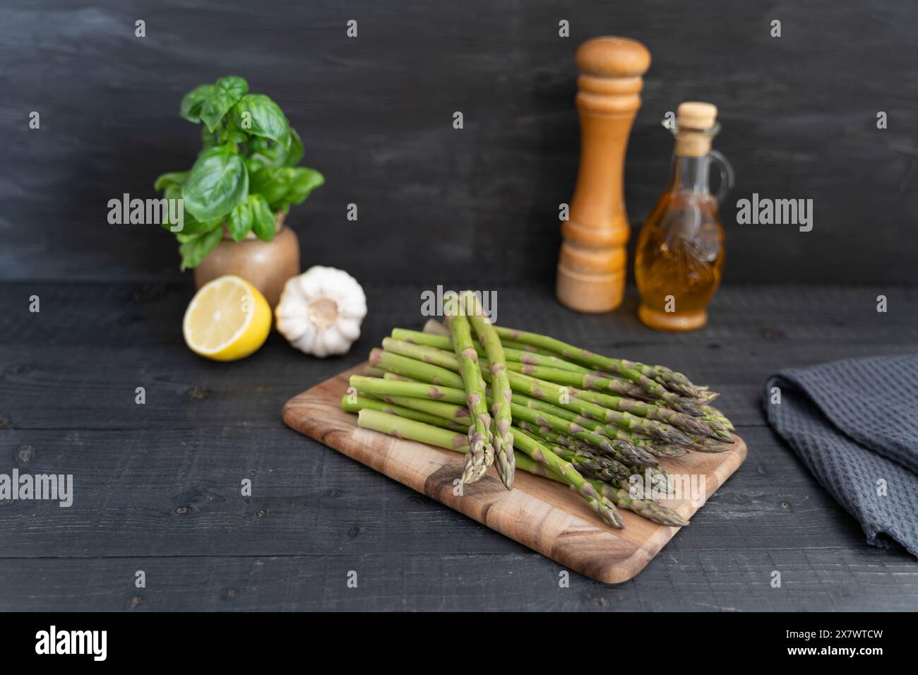 Contro una parete nera alcuni gambi di asparagi verdi freschi su un tagliere in legno Foto Stock