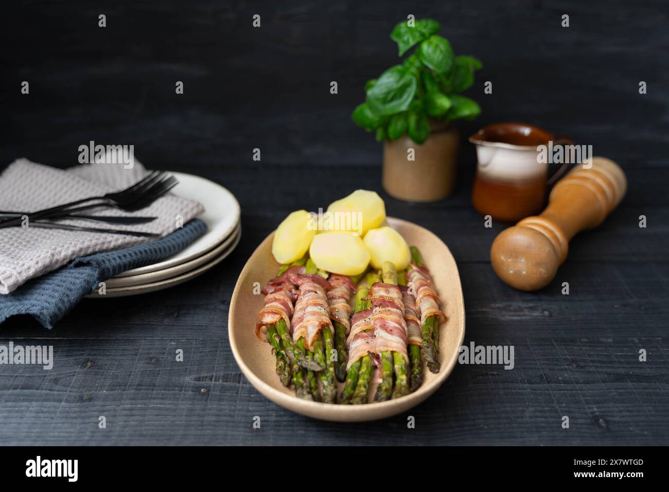 Asparagi verdi cotti avvolti nella pancetta e serviti con patate bollite su splendidi piatti beige su sfondo scuro Foto Stock
