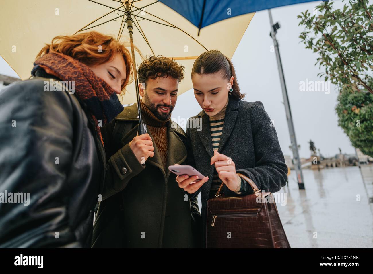 Uomini d'affari che collaborano e discutono di un progetto all'aperto sotto la pioggia, usando un ombrello come simbolo del lavoro di squadra e della resilienza. Foto Stock