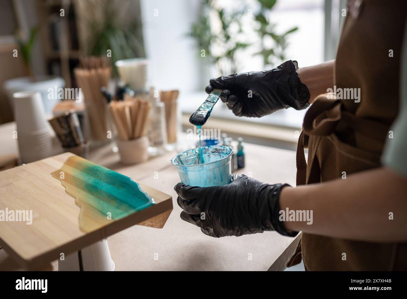 L'artista donna versa resina epossidica e la spalma di bastone su tavola di legno, utilizzando la tecnica dell'arte liquida Foto Stock