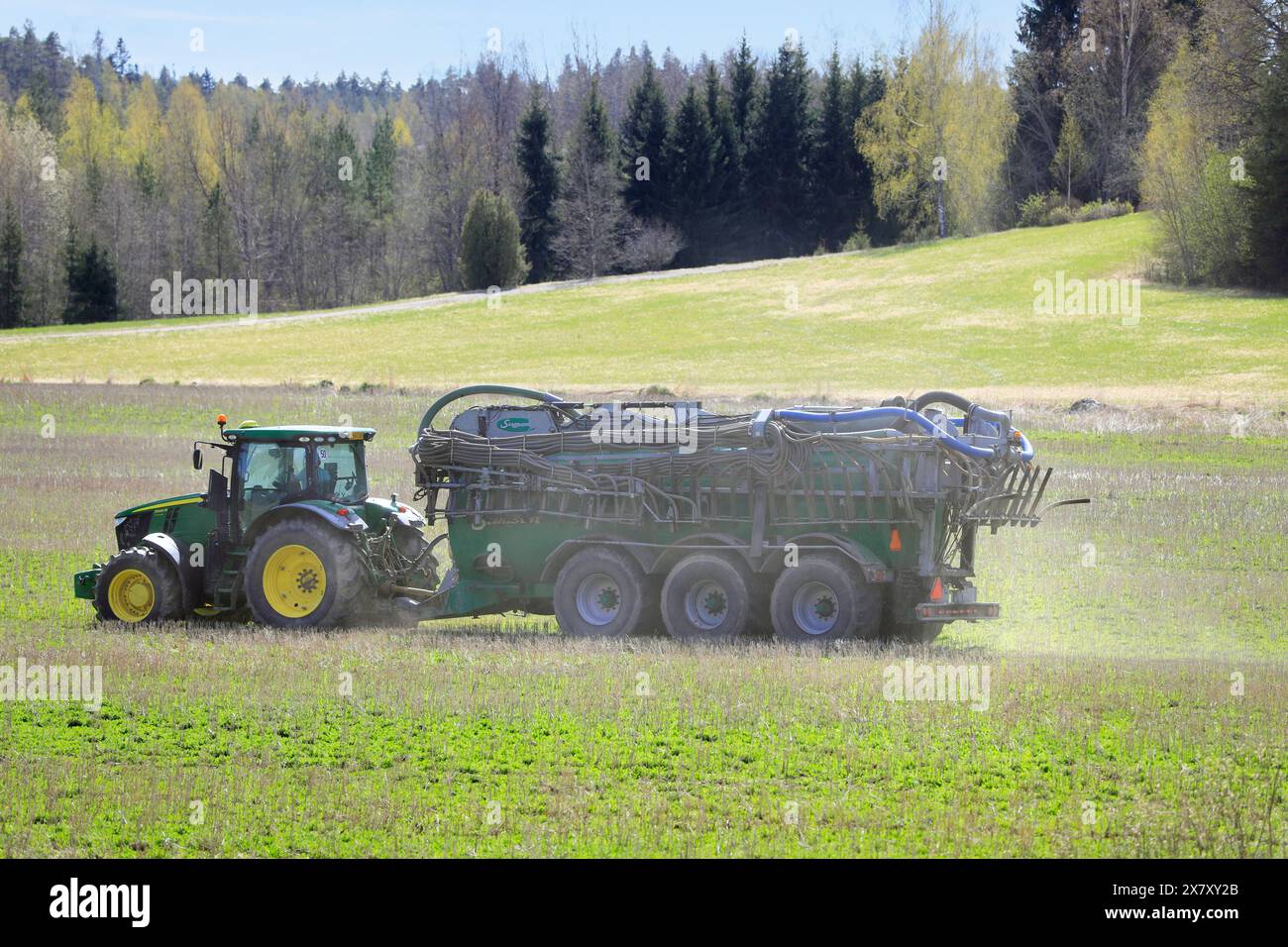 Trattore John Deere 7230R e autocisterna per liquami Samson PG nel campo stoppie per iniettare concime liquido per la fertilizzazione. Paimio, Finlandia. 10 maggio 2024. Foto Stock