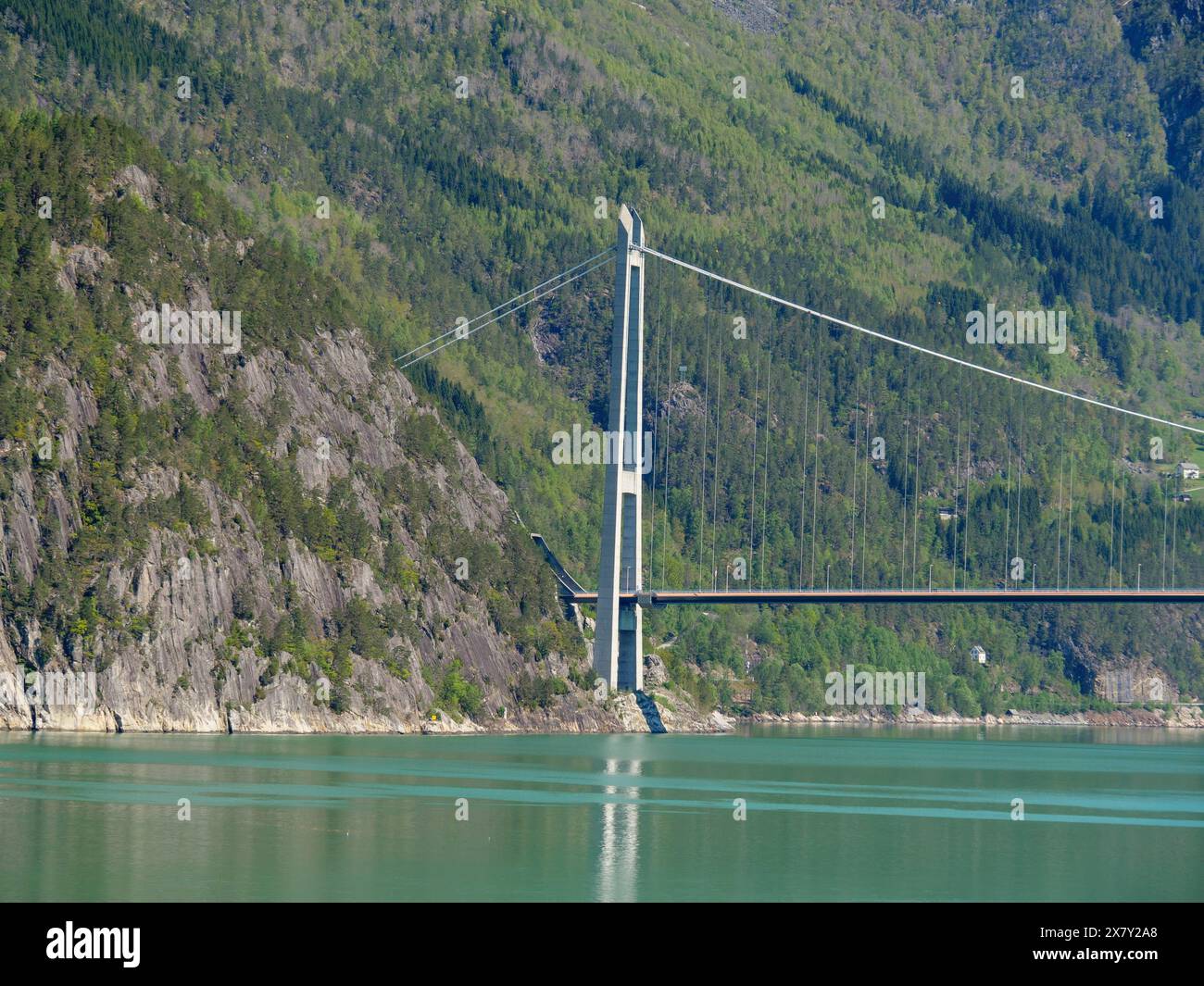 Imponente ponte sull'acqua verde brillante, incorniciato da ripide montagne boscose sotto un cielo blu, ponte in un fiordo con montagne innevate e verde Foto Stock