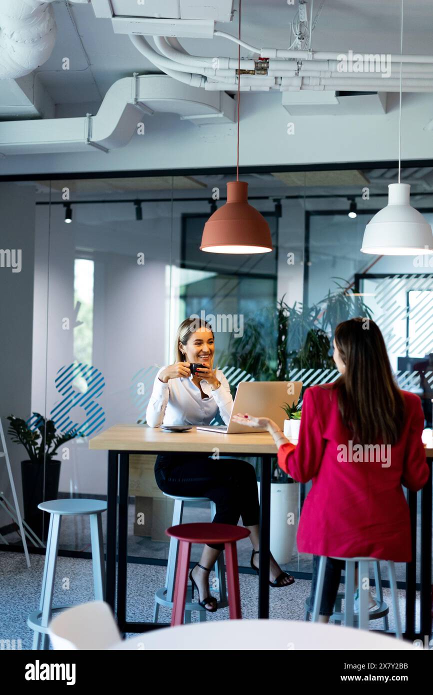 Due professionisti conversano su un moderno tavolo da ufficio, circondato da un design elegante e luce naturale, favorendo un ambiente produttivo e creativo Foto Stock