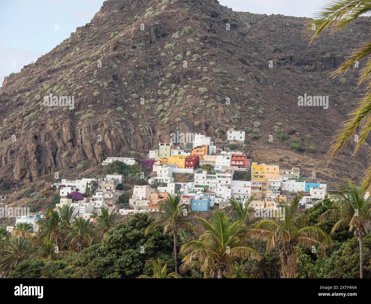 Piccolo villaggio con case colorate su una montagna rocciosa, circondato da palme e vegetazione lussureggiante, montagne e valli su un'isola nell'Atlan Foto Stock