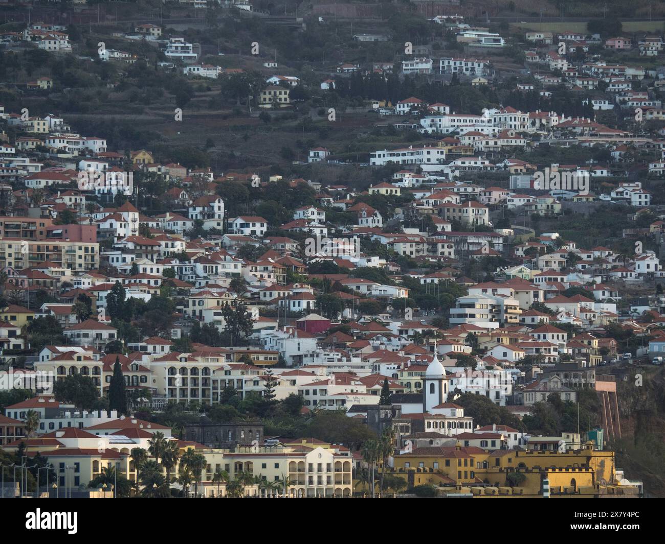 Una vista della città con molte case sparse su una collina, catturate al crepuscolo, nuvole su alte montagne con piccoli villaggi di montagna nella valle, Madeira, P. Foto Stock