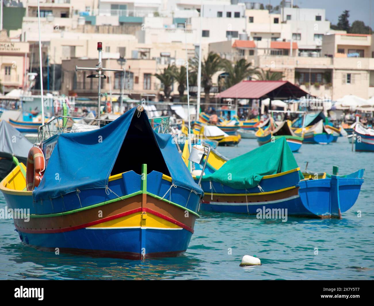 Colorate barche da pesca nel porto, in parte ricoperte di teloni, di fronte a una città costiera con il sole, molte colorate barche da pesca in una Foto Stock