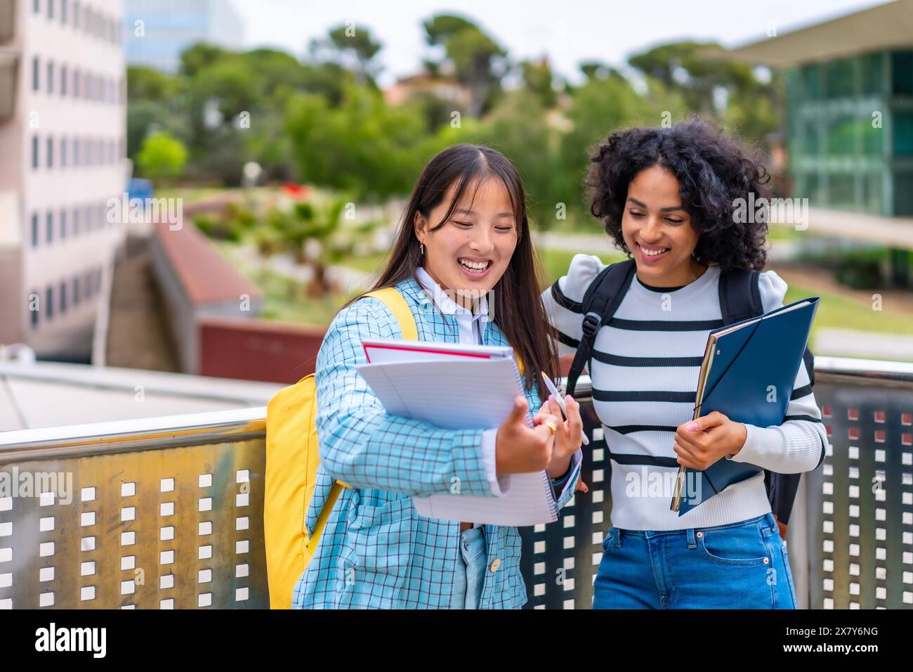 Due giovani e sorridenti studenti multietnici che leggono appunti fuori dal campus universitario Foto Stock