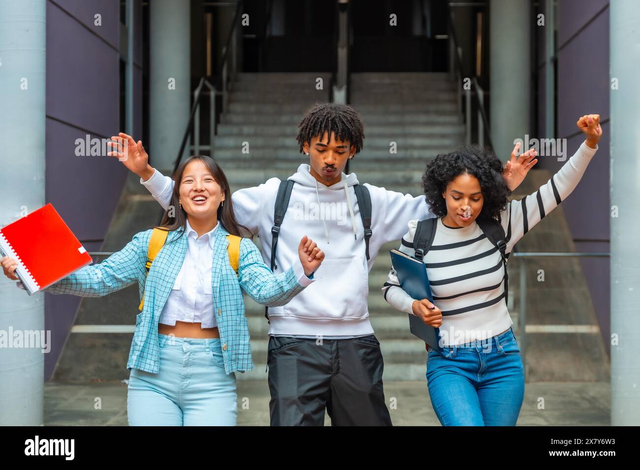 Tre studenti di sesso maschile e femminile multietnico che si divertono a festeggiare e ballare fuori dall'università Foto Stock