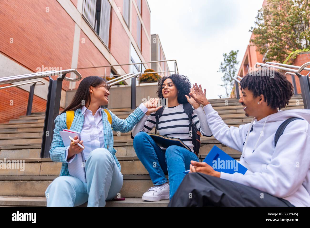 Tre studenti multietnici che lavorano in alto mentre si siedono su alcune scale del campus universitario Foto Stock