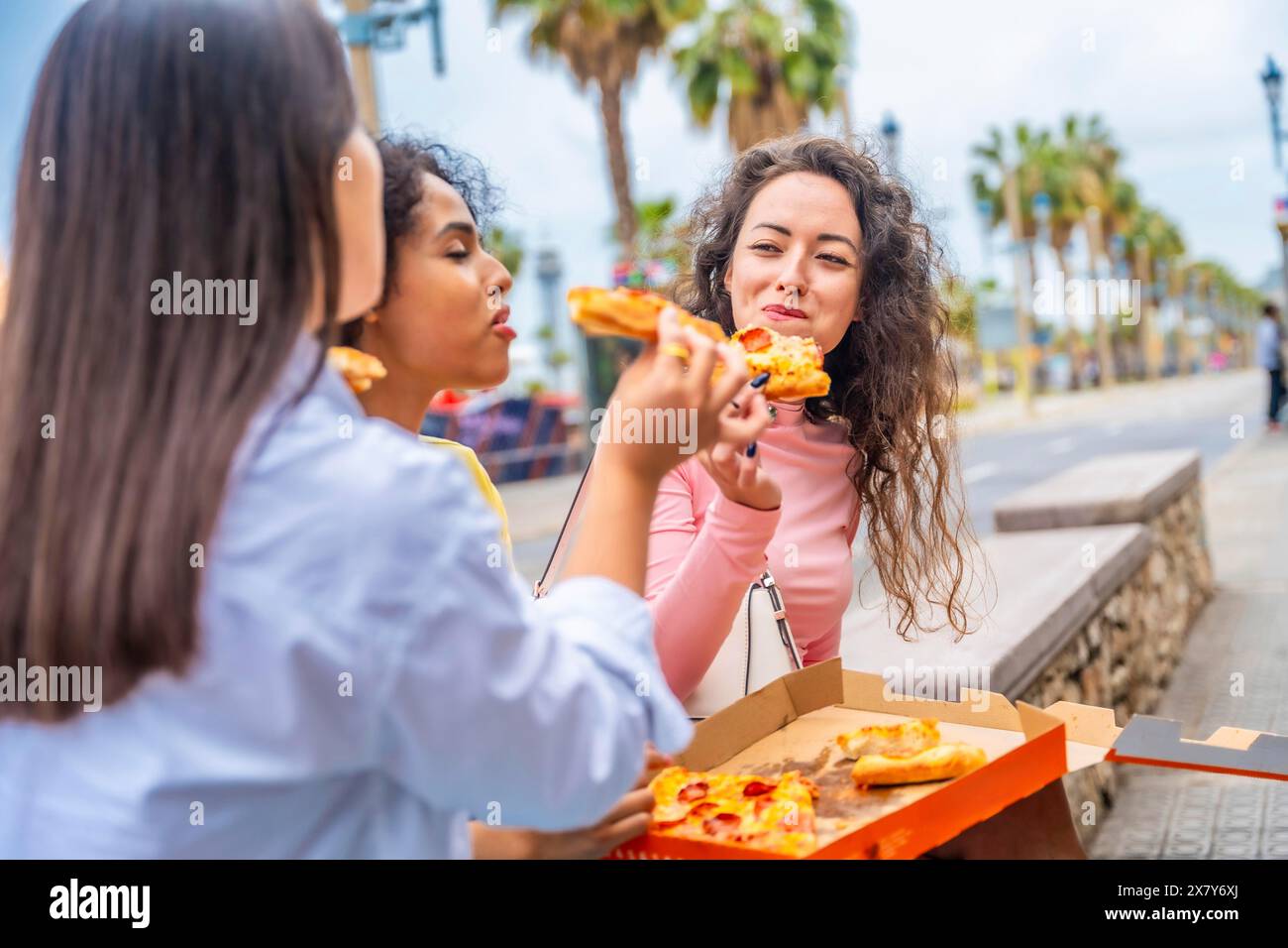 Tre turisti diversi che chiacchierano e condividono la pizza seduti in strada Foto Stock