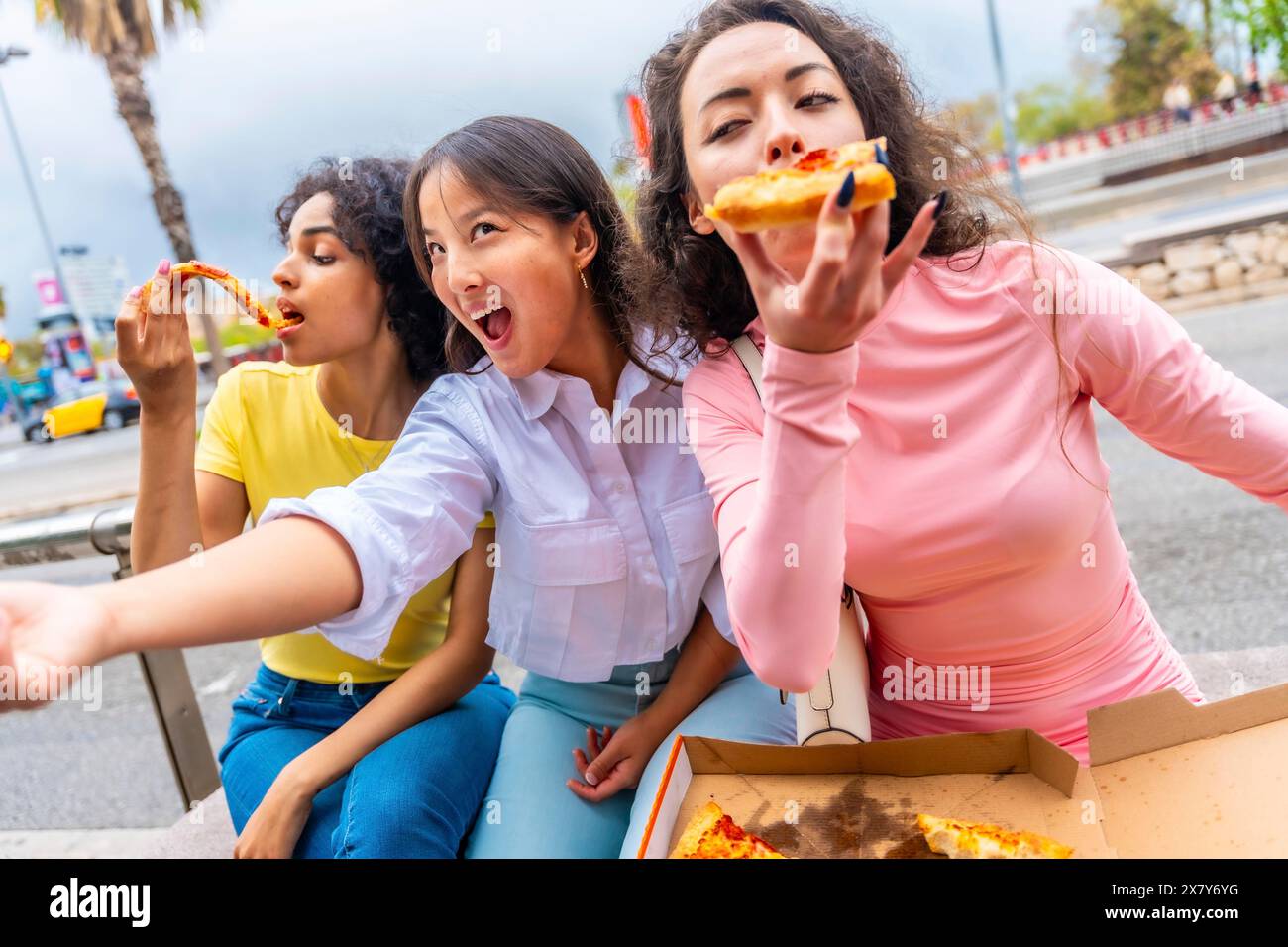 Felici amiche multietniche che si fanno selfie mentre condividono la pizza per strada Foto Stock
