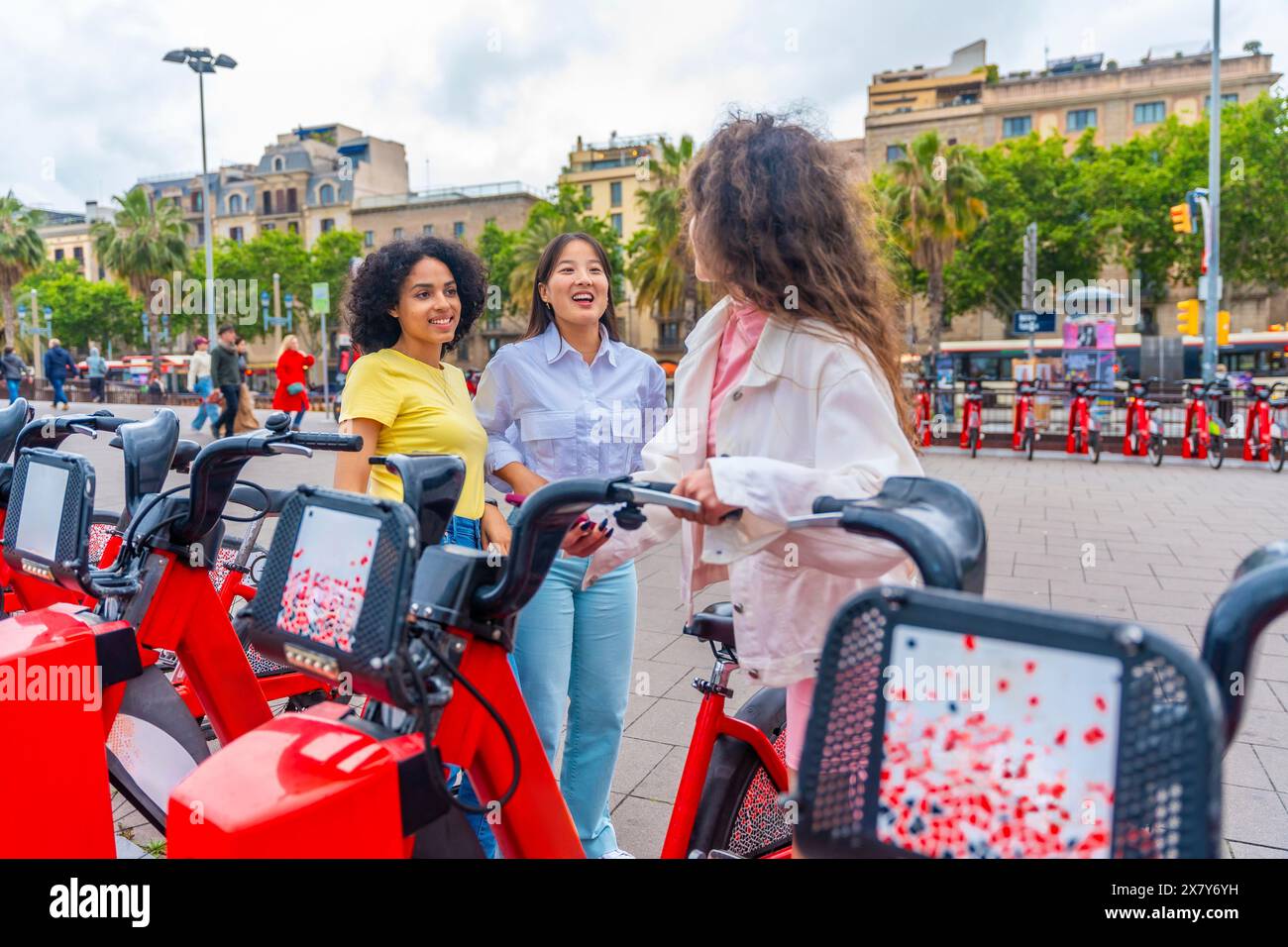 Tre diverse amiche affittano biciclette pubbliche nella città di Barcellona Foto Stock