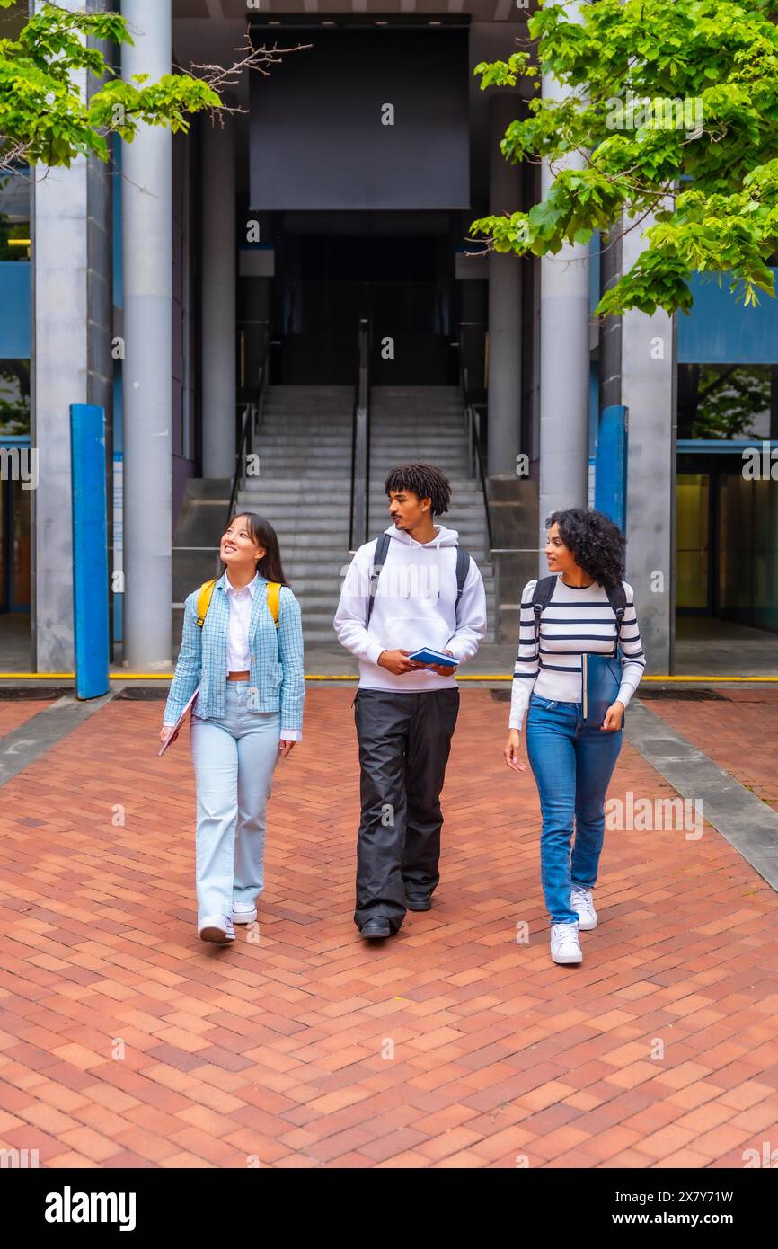 Foto verticale di tre studenti multirazziali che camminano lungo il campus dell'università Foto Stock