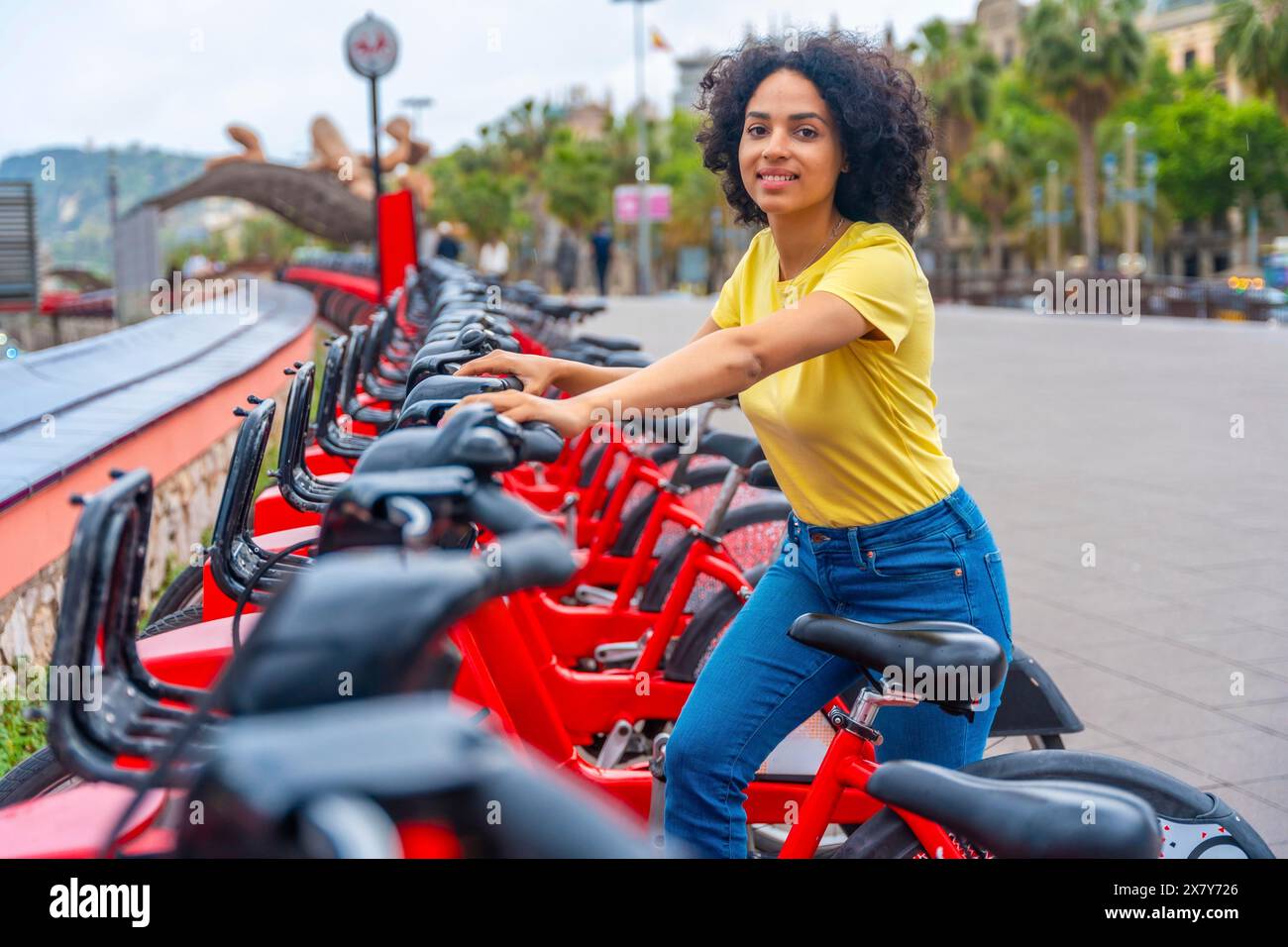 Ritratto di una giovane donna latina sorridente alla macchina fotografica mentre utilizza il servizio di noleggio bici pubblico Foto Stock