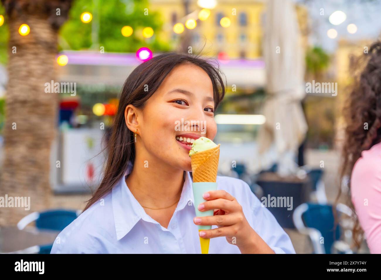 Primo piano di una donna cinese sorridente che mangia un gelato in città Foto Stock
