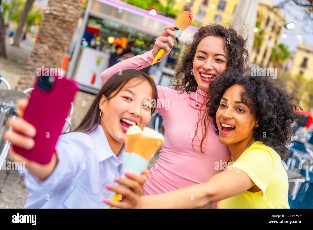XRThree amiche multietniche che si fanno selfie mentre mangiano gelati in città Foto Stock