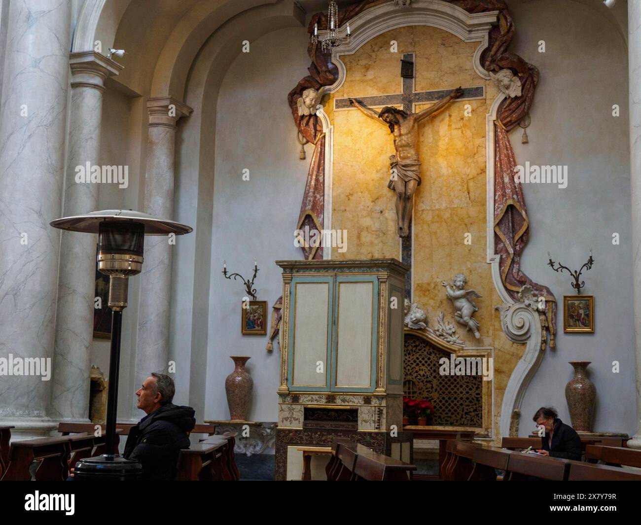 L'interno solenne di una chiesa con un crocifisso sopra l'altare, illuminazione calda e persone che pregano sulle panchine, Catania, italia, 3 febbraio 2024, 3 da Foto Stock