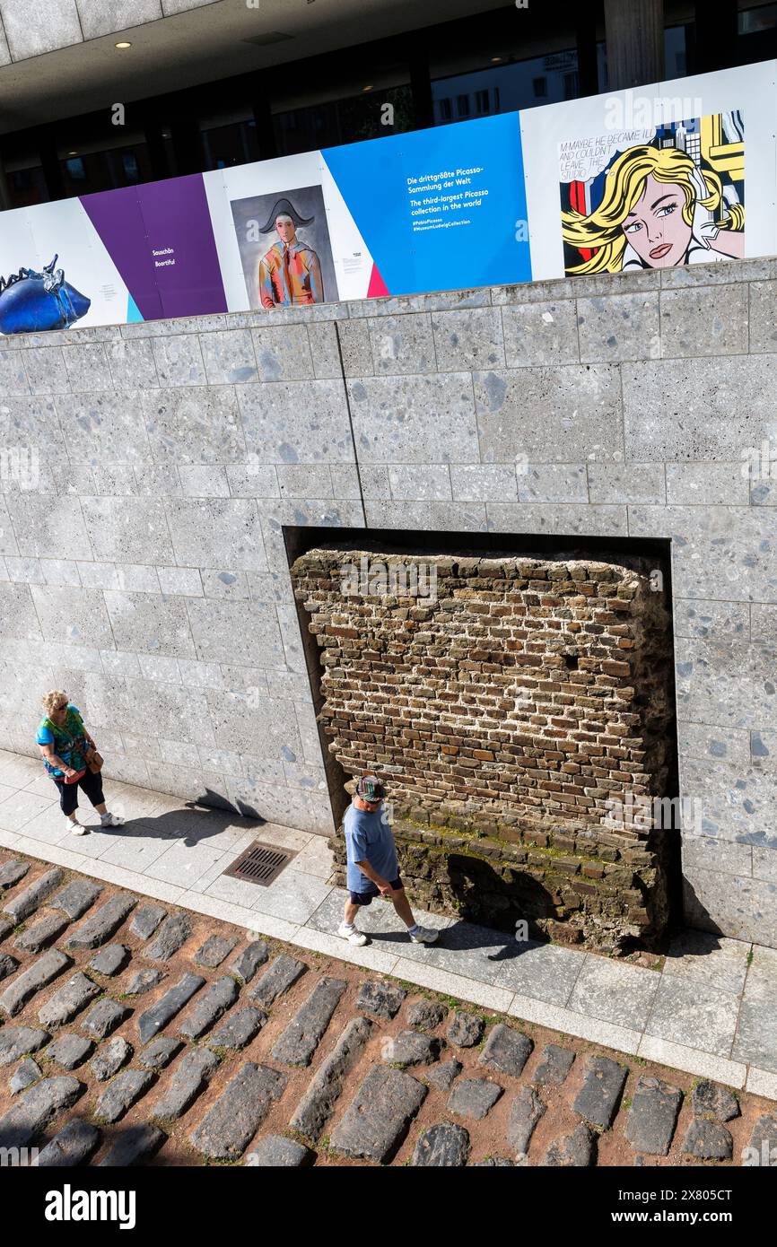 Coppia che cammina lungo la vecchia strada del porto romano vicino alla cattedrale, sopra ci sono le foto su una recinzione di costruzione del Museo Romano-Germanico di Colonia, Foto Stock