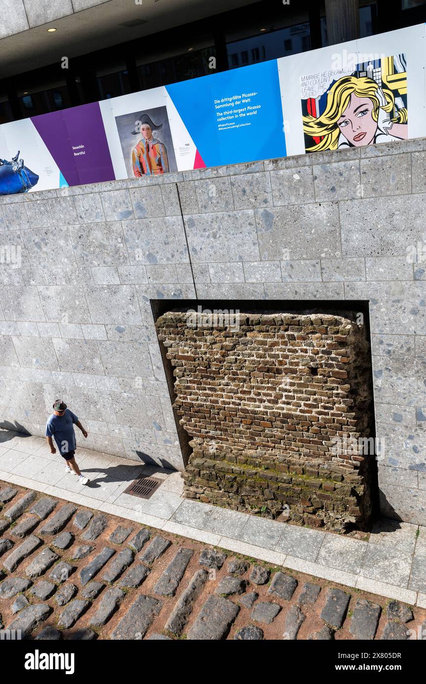 Uomo che cammina lungo la vecchia strada del porto romano vicino alla cattedrale, sopra ci sono le foto su una recinzione di costruzione del Museo Romano-Germanico di Colonia, Ger Foto Stock