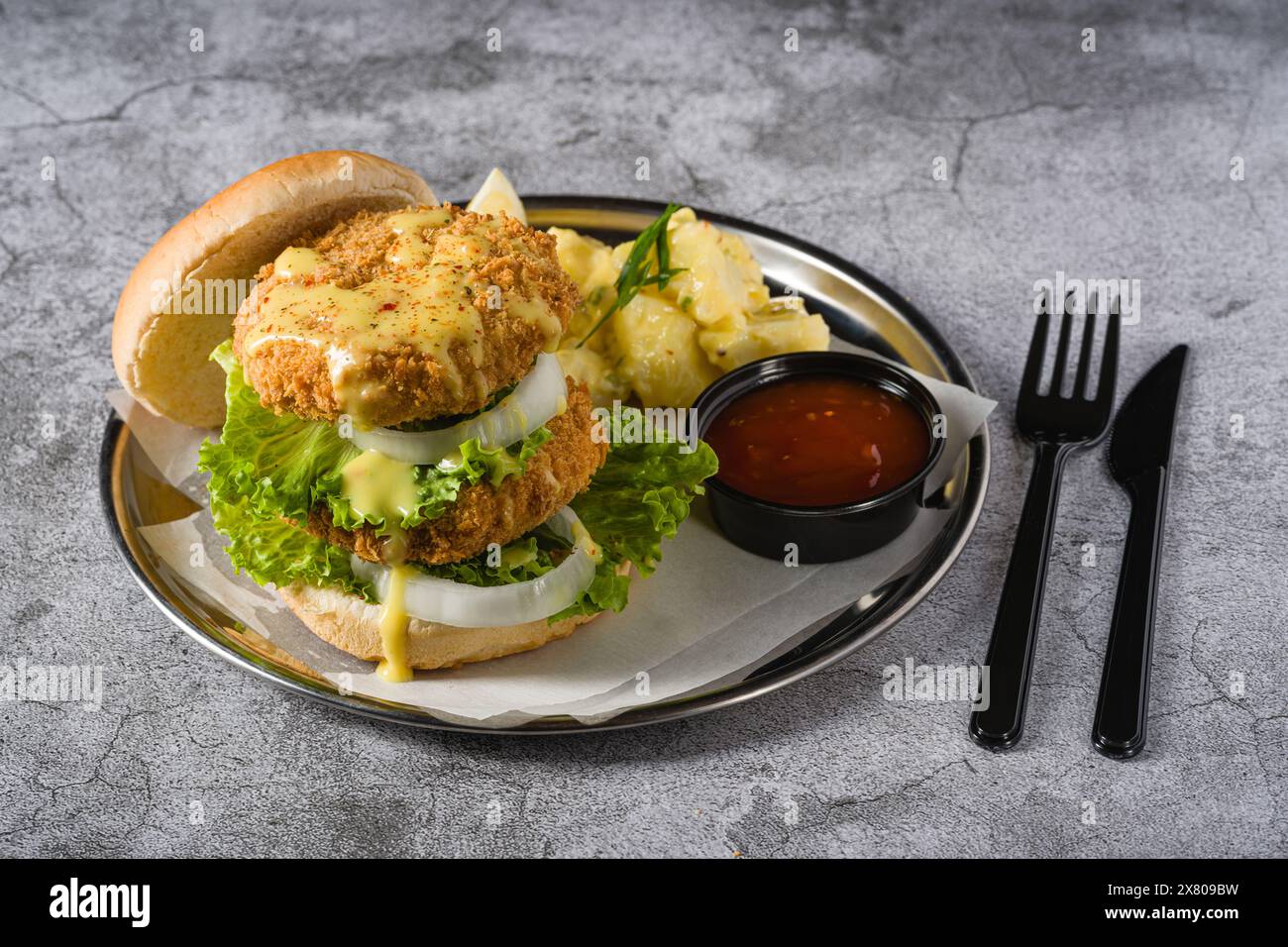 Doppio hamburger di pesce con insalata di patate su un piatto di metallo Foto Stock