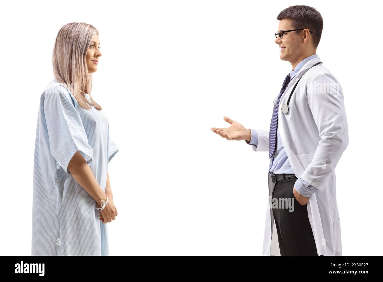 Medico di sesso maschile che parla con una giovane donna in un abito paziente isolato su sfondo bianco Foto Stock