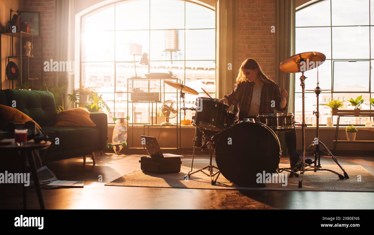 Giovane donna che suona i tamburi durante una prova della band in un Loft Studio con luce calda al giorno. La batterista Girl fa pratica prima di un concerto dal vivo sul palco con altri musicisti. Foto Stock