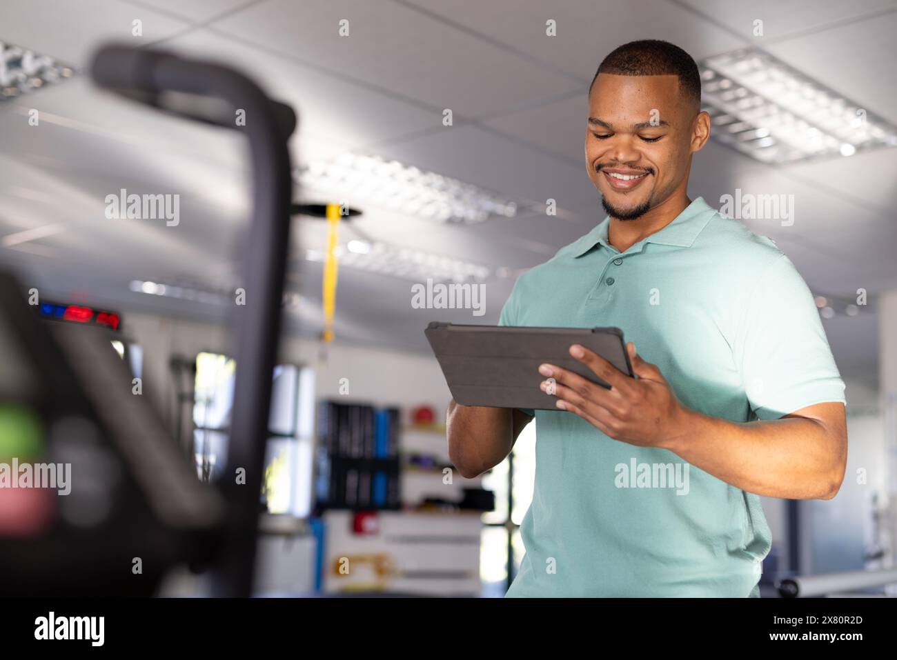 Un fisioterapista birazziale maschile che tiene una compressa presso il centro di riabilitazione della palestra Foto Stock
