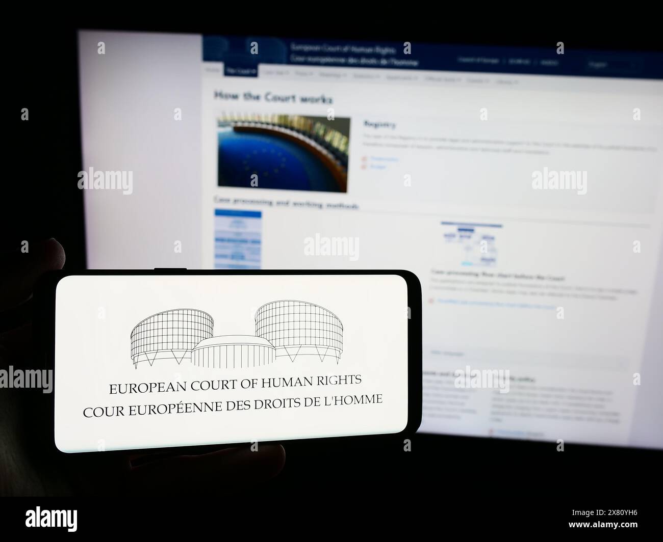 Persona che possiede uno smartphone con il logo del tribunale internazionale della Corte europea dei diritti dell'uomo (CEDU) davanti al sito web. Mettere a fuoco il display del telefono. Foto Stock