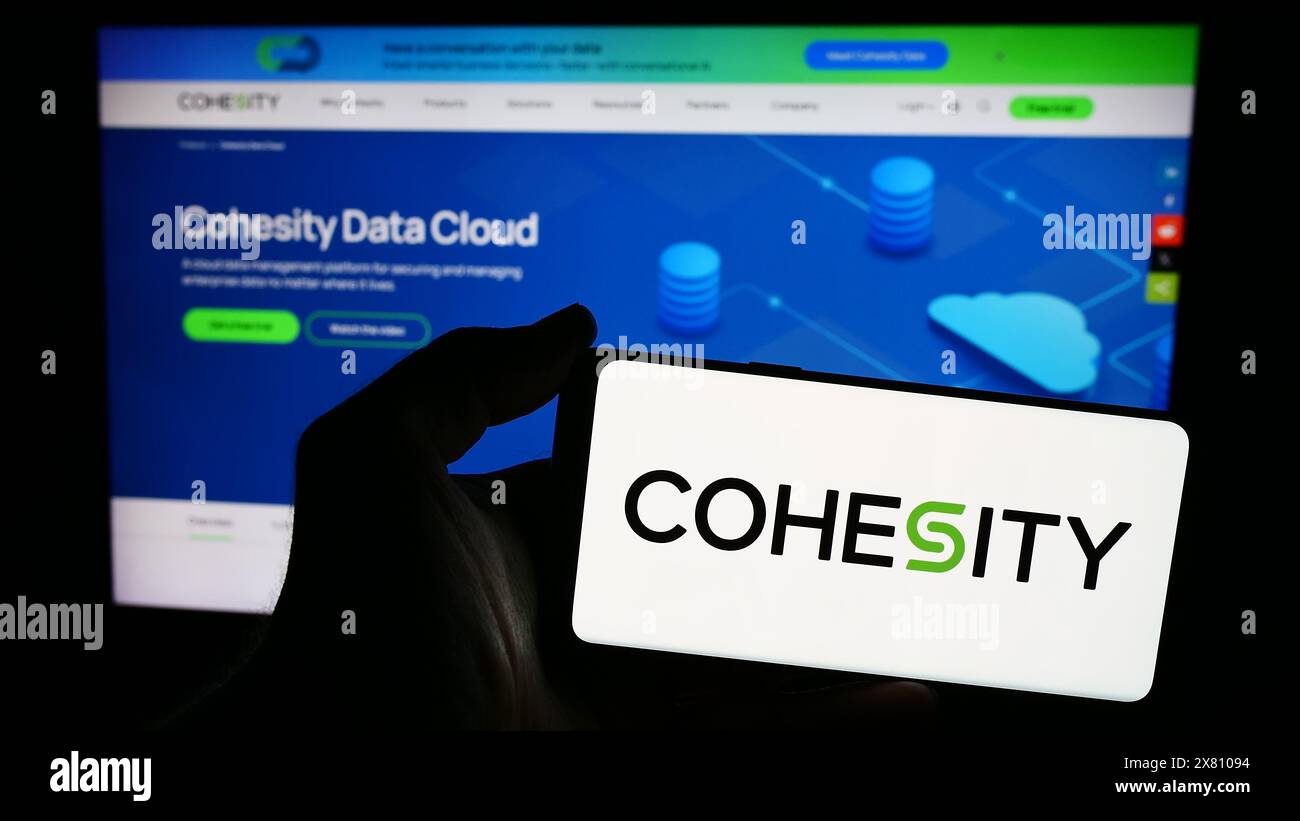 Persona con smartphone con logo della società statunitense di gestione dati Cohesity Inc. Davanti al sito Web. Mettere a fuoco il display del telefono. Foto Stock