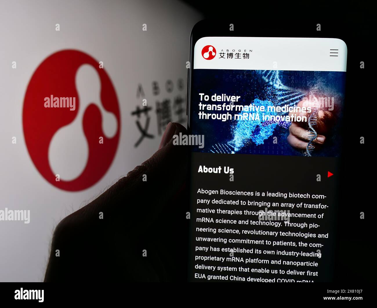 Persona che detiene il cellulare con il sito web della società cinese Suzhou Abogen Biosciences Co. Ltd. Di fronte al logo. Messa a fuoco al centro del display del telefono. Foto Stock