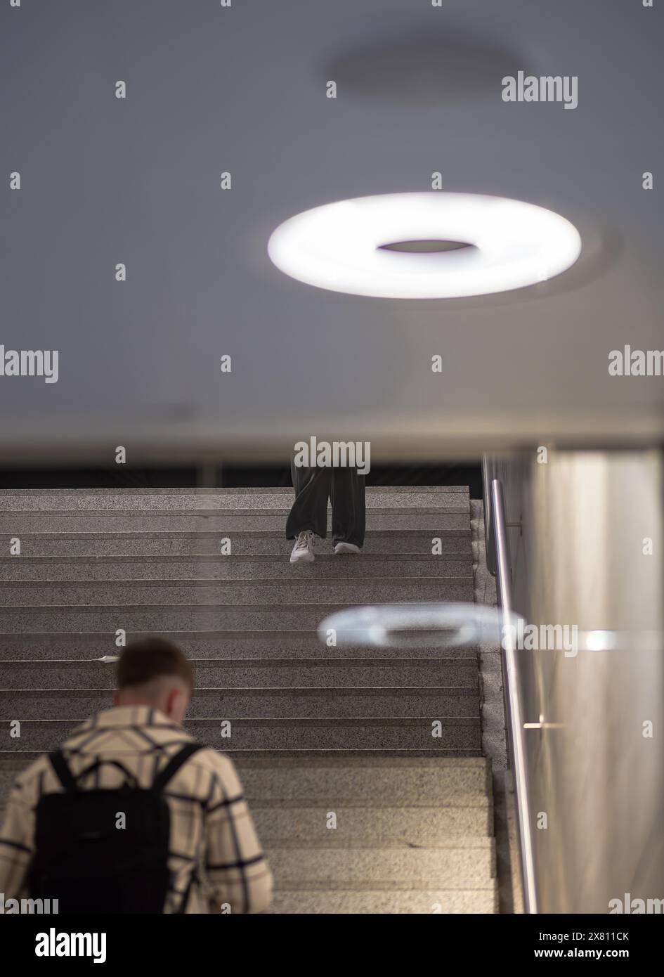 Zurigo, Svizzera - 16 maggio 2024: Una scena urbana moderna in uno spazio pubblico con scale, persone in abbigliamento casual, illuminazione circolare luminosa e un neutr Foto Stock