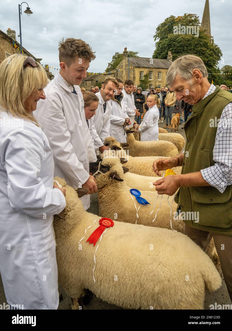 Giudice che colloca rosoni sulle pecore vincitrici mentre i loro giovani proprietari, vestiti con cappotti bianchi, guardano alla Masham Sheep Fair, North Yorkshire, Regno Unito Foto Stock