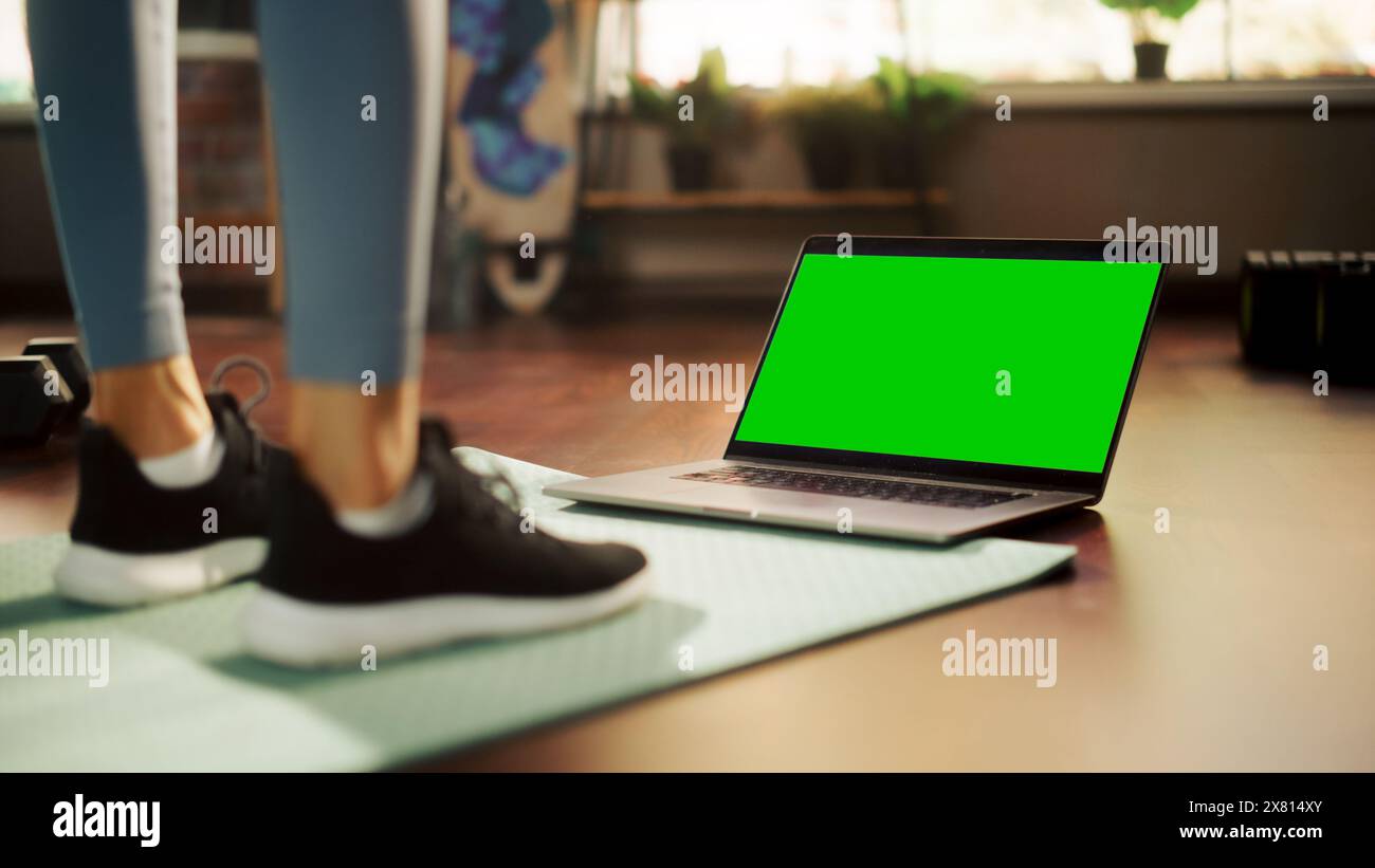 Allenamento femminile, guardare Trainer su un notebook, tramite video tutorial online con Chroma Green Screen. Atletica che utilizza l'abbonamento fitness ai servizi di streaming. Ripresa in basso di gambe e notebook Foto Stock
