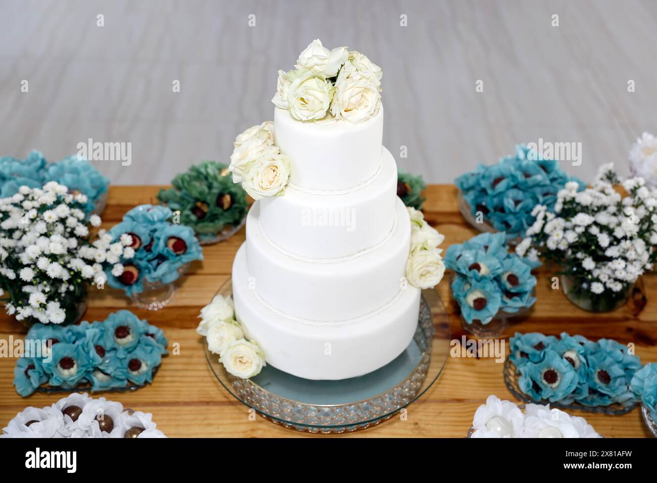 torta bianca di compleanno con quattro parti, con fiori bianchi e vari dolci sul tavolo Foto Stock