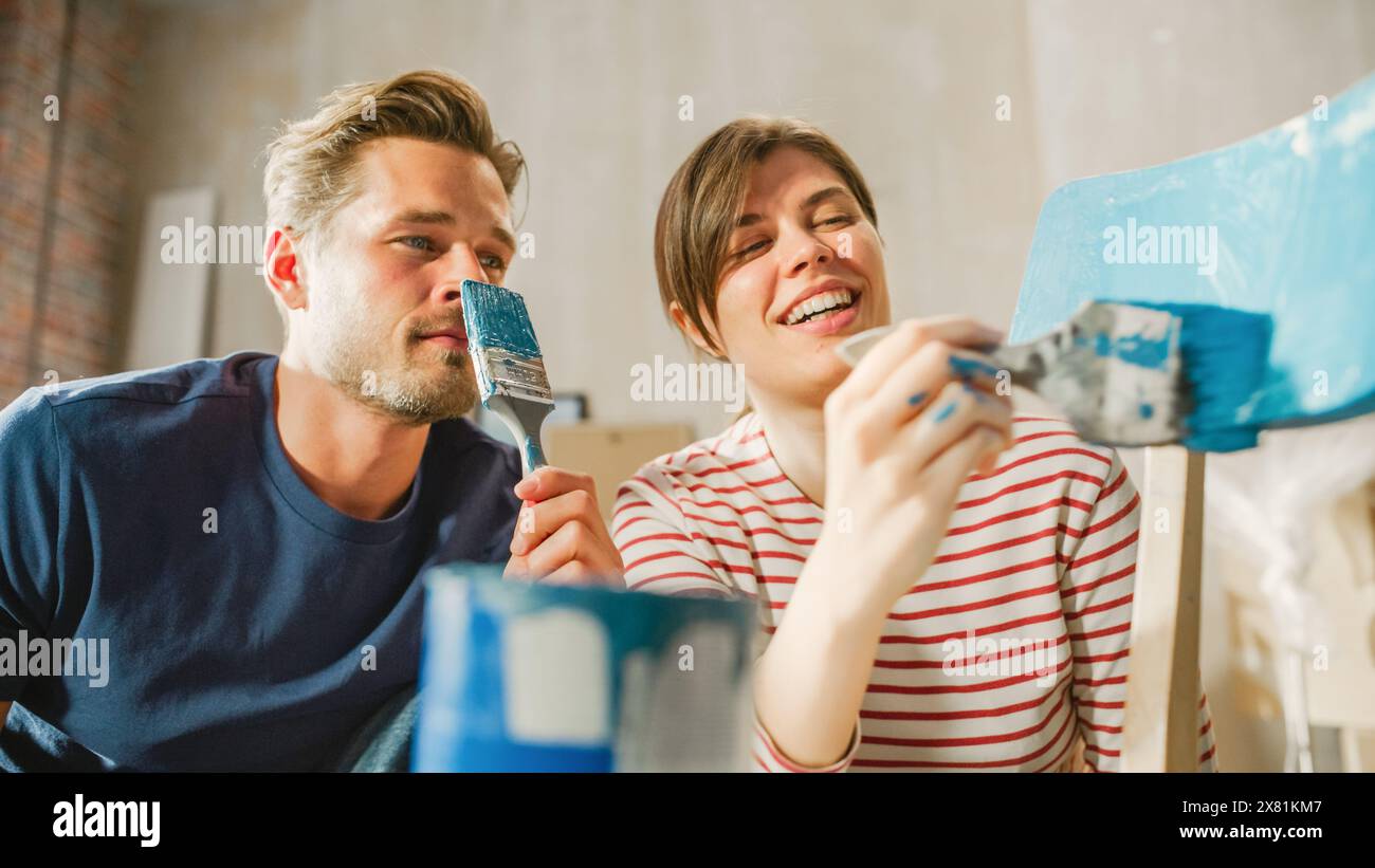 Famiglia che si trasferisce in casa e ristrutturazioni di casa: Sedia per mobili di pittura di coppia per casa accogliente. Fidanzato e fidanzata rendono l'appartamento confortevole con Art, Color. Sorrisi e felicità. Foto Stock