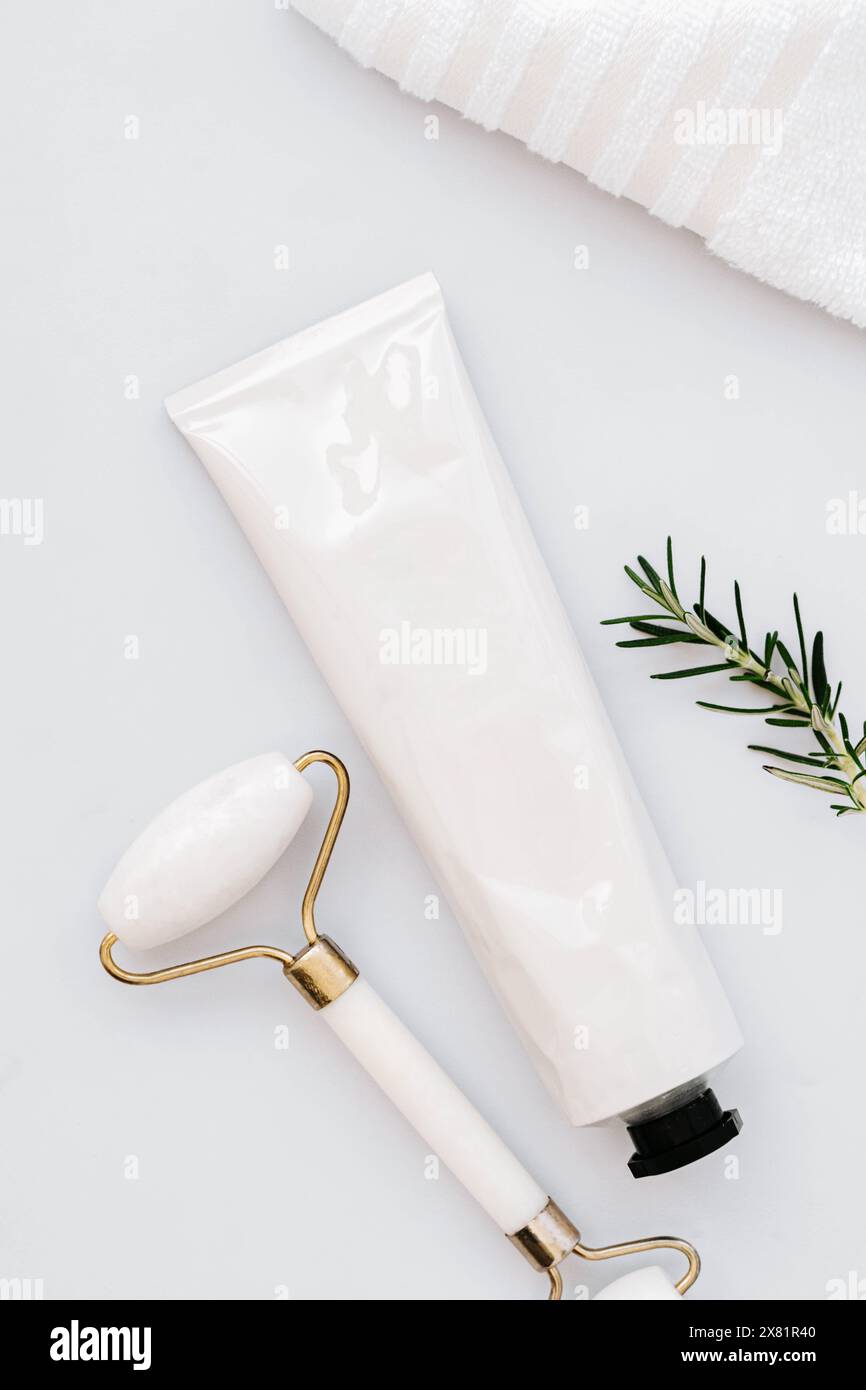 Primo piano di una provetta bianca senza etichetta e rullo facciale su sfondo bianco del tavolo in marmo. Concetto minimo di bottiglia di crema facciale, gel, mockup balsamo. Foto Stock