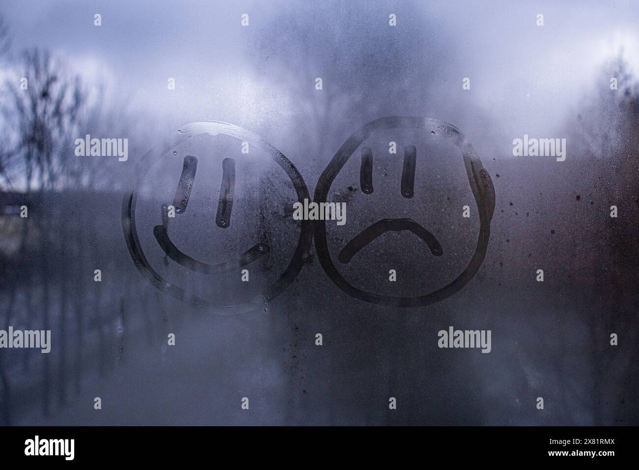 faccia sorridente e triste faccia sorridente dipinta su vetro nebbioso, sfondo blu freddo, diversità Foto Stock