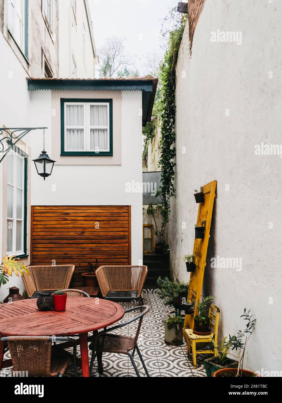 Un intimo cortile urbano privato con eleganti sedie, un tavolo in legno rosso e un pavimento piastrellato a motivi geometrici che invita al relax. Foto Stock