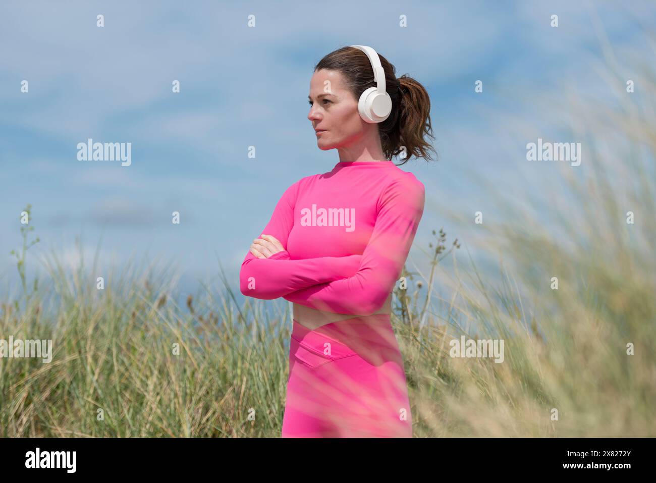 Donna sportiva che ascolta la musica, indossa abiti sportivi rosa contro il cielo blu Foto Stock