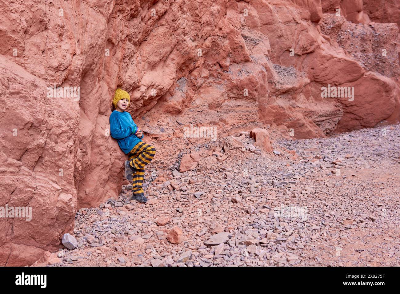 Ragazzo latino appoggiato a una formazione rocciosa che posa mentre guarda la macchina fotografica durante una vacanza in famiglia nel nord dell'Argentina. Foto Stock