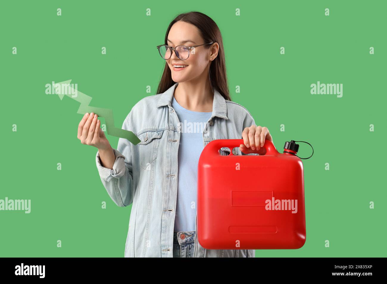 Giovane donna con tanica e freccia su sfondo verde. Concetto di aumento dei prezzi Foto Stock