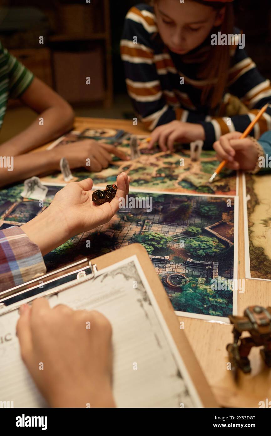 Mano di una ragazza giovane che tiene un gruppo di dadi prima di lanciarli a bordo con una foto della foresta magica durante il gioco da tavolo Foto Stock