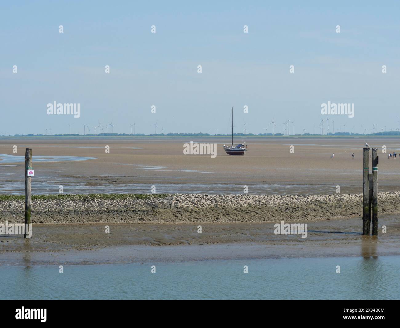 Una singola barca si trova su un'ampia area sabbiosa con bassa marea e bassa marea in un piccolo porto su un'isola del Mare del Nord con navi a vela, baltrum, Germania Foto Stock