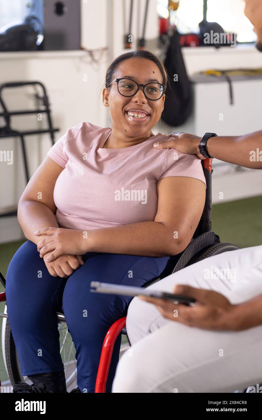 Una paziente paraplegica birazziale in sedia a rotelle in un centro di riabilitazione in palestra, sorridente Foto Stock