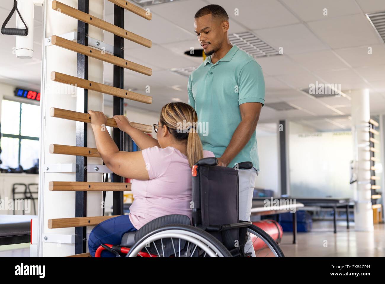 Una paziente birazziale paraplegica che raggiunge i bar del centro di riabilitazione della palestra Foto Stock