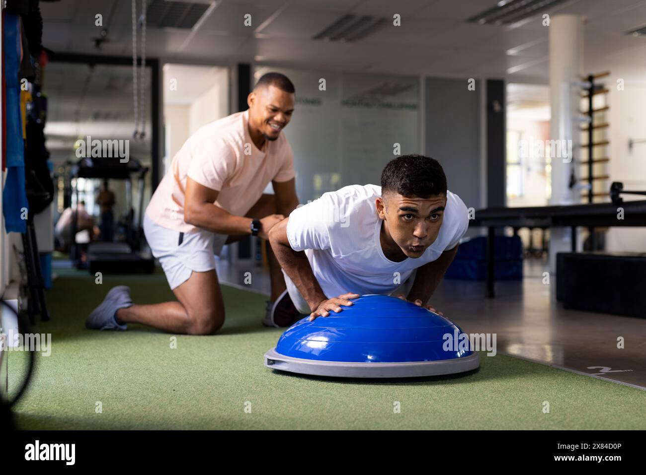Al centro di riabilitazione, terapista maschile birazziale che aiuta il paziente con esercizi di cupola di equilibrio Foto Stock